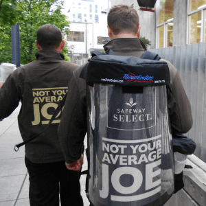 Two men walking with a jug of coffee on their back