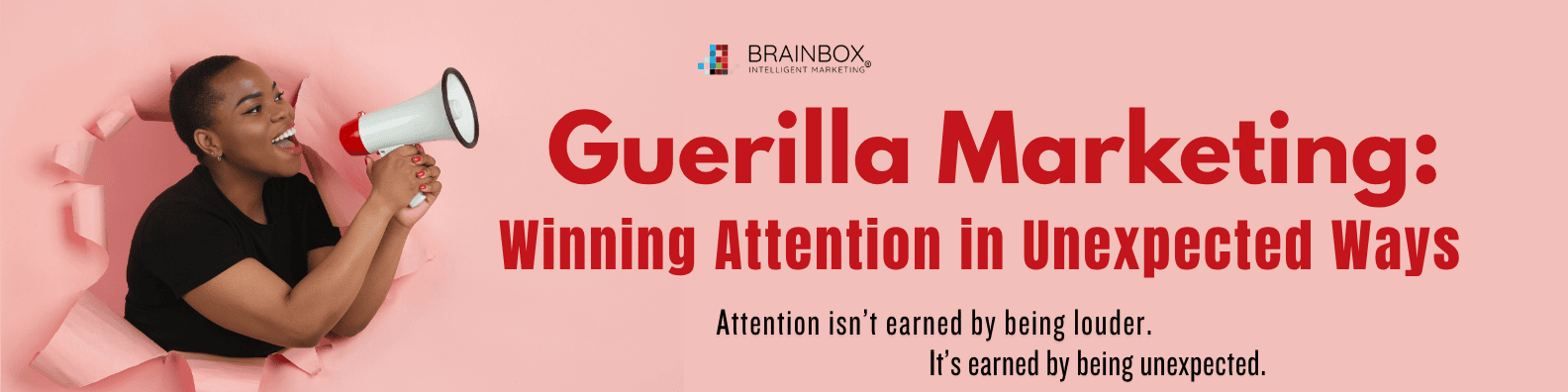 BrainBox Intelligent Marketing graphic featuring a woman breaking through a pink paper wall holding a megaphone beside the headline “Guerilla Marketing: Winning Attention in Unexpected Ways.