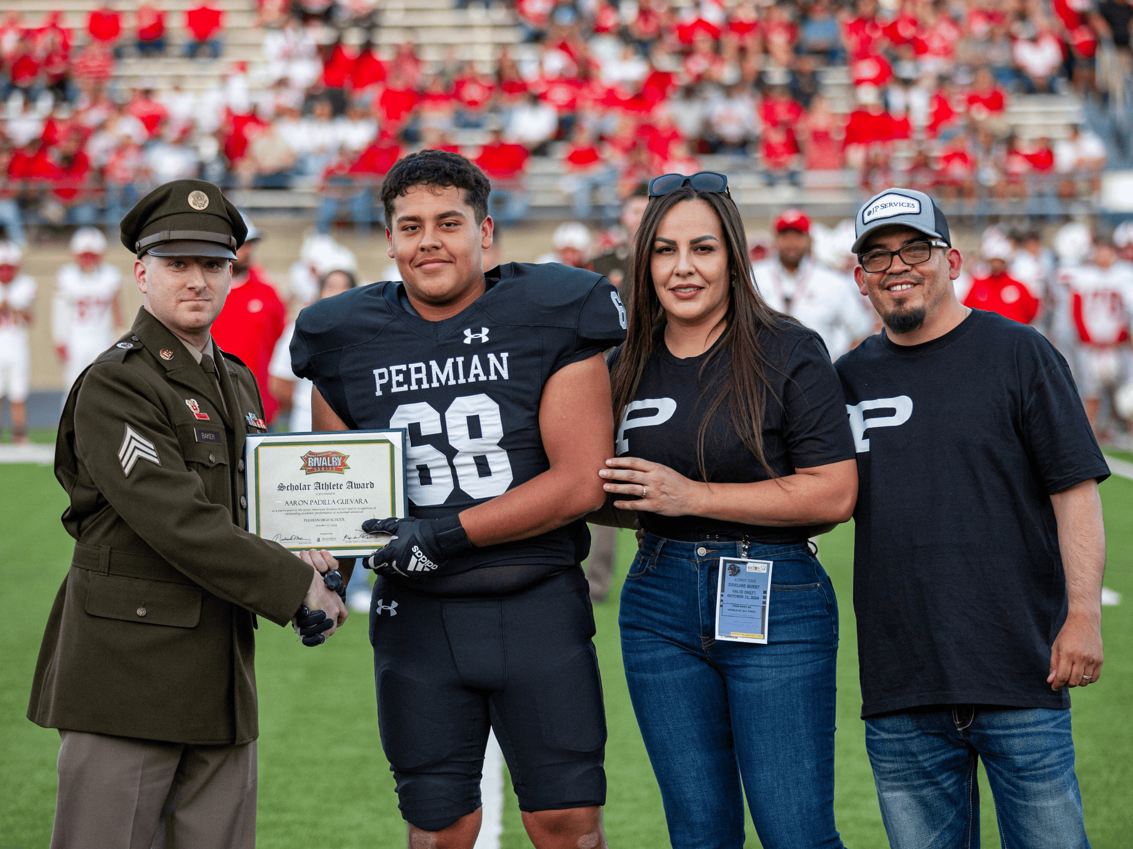Football playing shaking hands with Army Soldier and holding a plaque. His mom and dad stand next to him.
